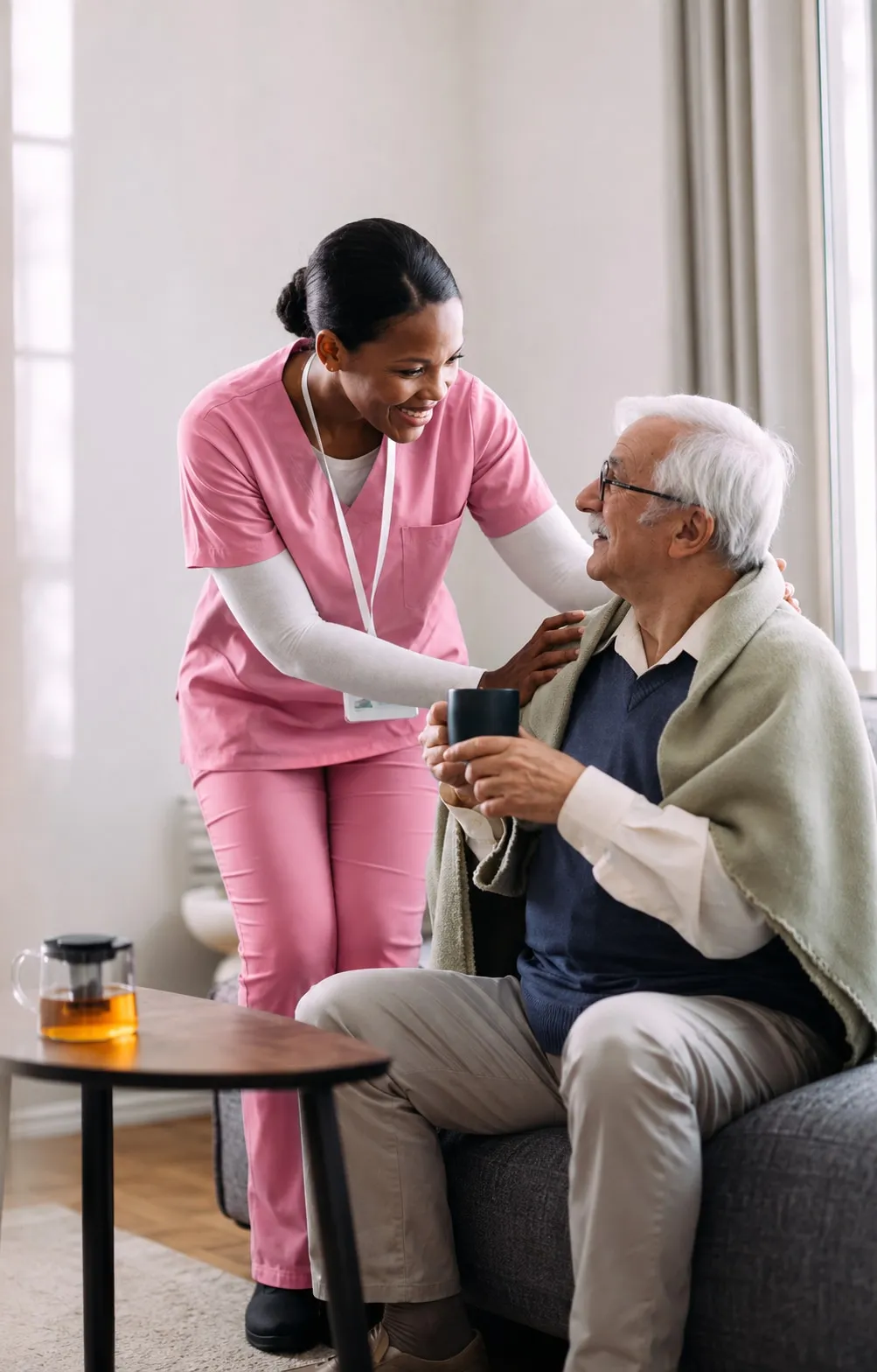 Une infirmière à domicile accompagne un patient âgé assis dans son salon.